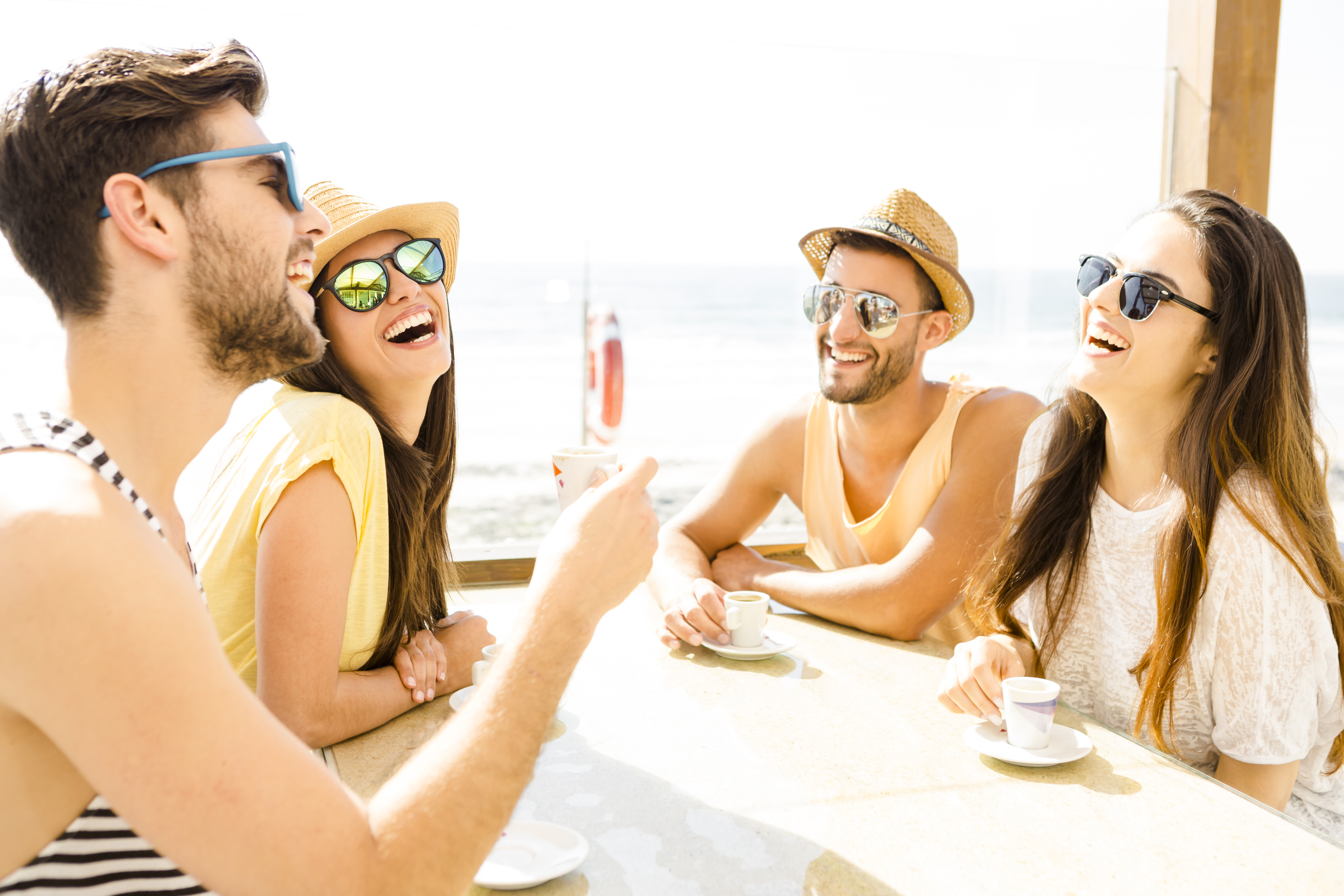 friends wearing sunglasses at beach cafe drinking coffee